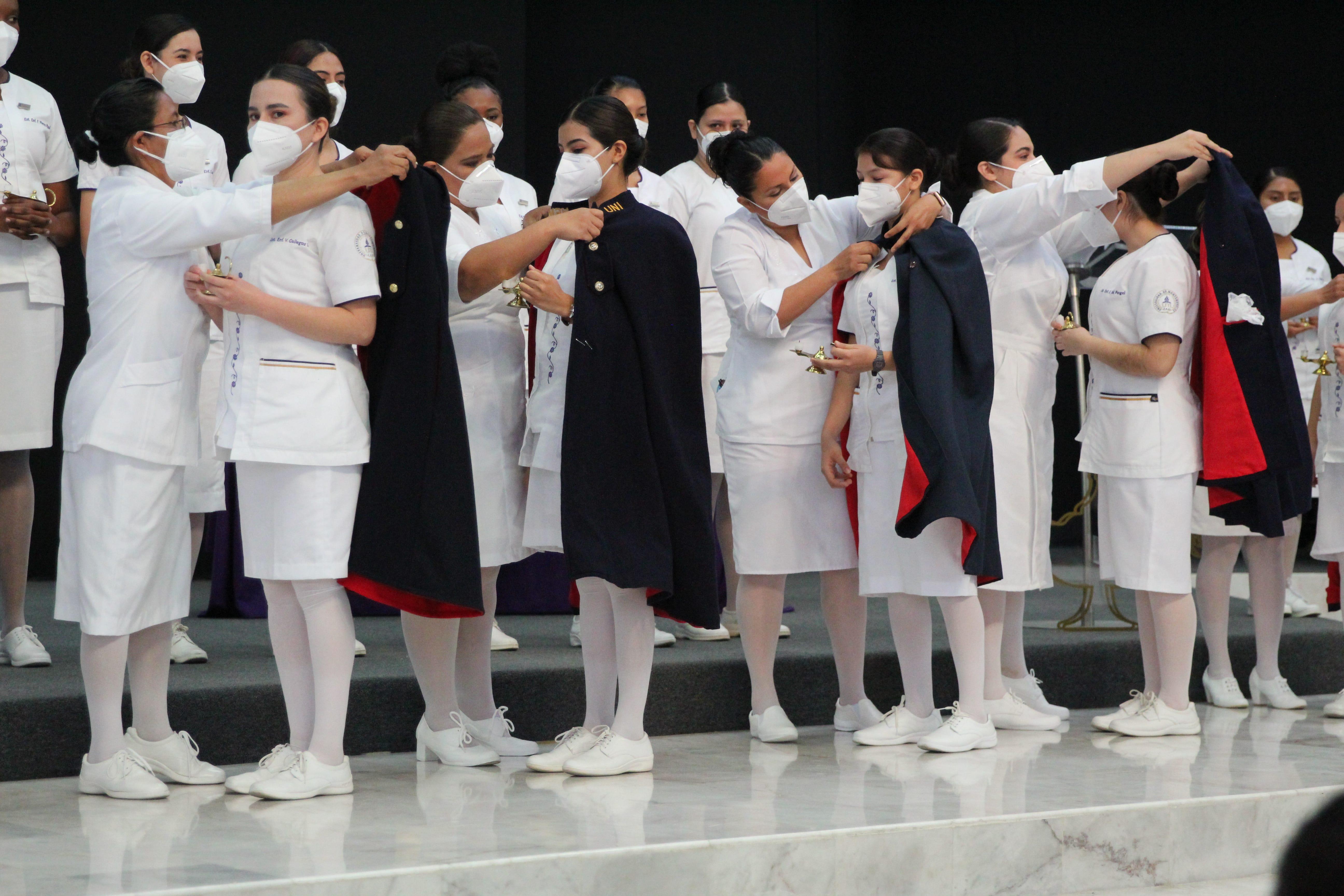 Las maestras invitadas por las alumnas de 4to. Año, son quienes colocan la capa a cada estudiante. Fotografía por: Comunicación Institucional.